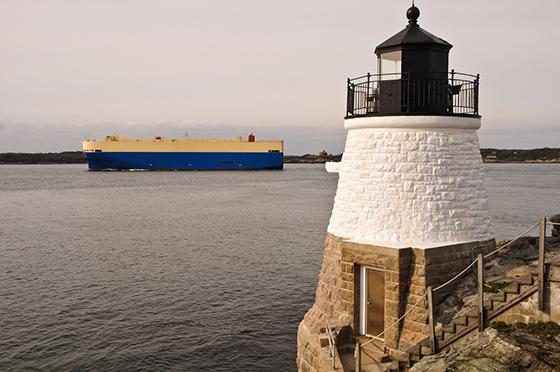 a lighthouse in foreground with container ship on calm waters in background