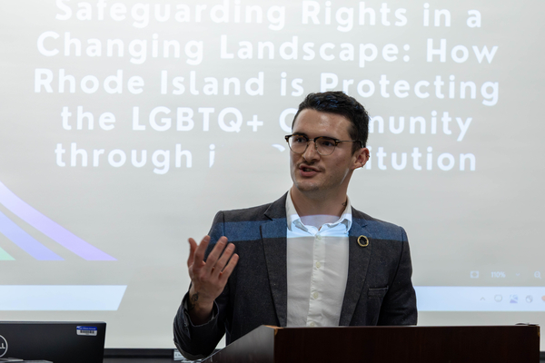 Male law student wearing eyeglasses, showing right hand gesture,  with a PPT slide behind him. 