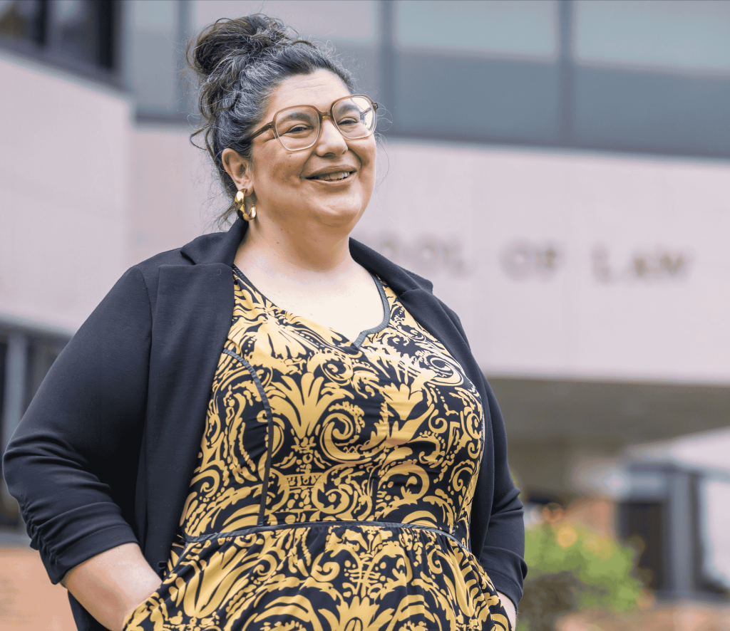Professor Nicole wearing glasses smiling gleefully with School of Law in the background