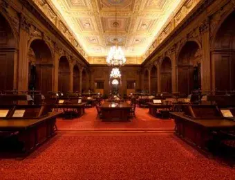 Supreme Court Library. Plush red carpet with large wooden tables and chairs lined on either side of an aisle.
