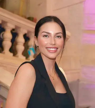 Female with hair up and black top smiling on camera with stairs in the background