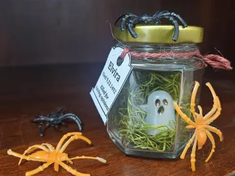 plastic orange spiders surround plastic ghost in a glass jar