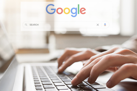 Hands typing on a keyboard with the Google logo and search bar above