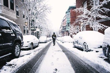 Man walking down middle of snow covered city street 