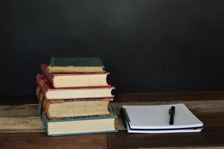 Stack of books next to white paper pad and pen