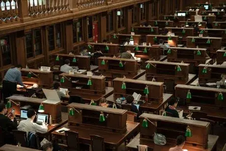 People sitting at desks in a library with laptops and books.