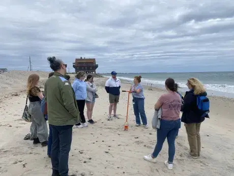 A small group of people standing up, gathered around in discussion, at a beach.