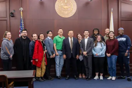 Group of students with guest speaker K. Jospeh Shekarchi pictured in the Hon. Bruce Selya Appellate Courtroom with the RWU Law school seal in the background.