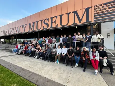 Students participating in the Civil Rights trip seated for a photo with The Legacy Museum on the background. 