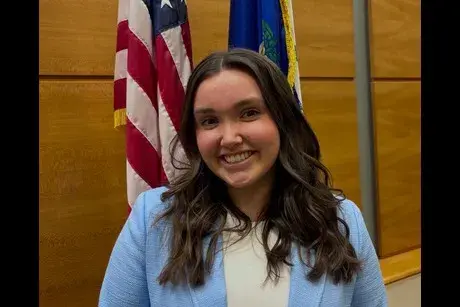Alexis (female student) close up with CT and US flags behind her, wearing light blue jacket