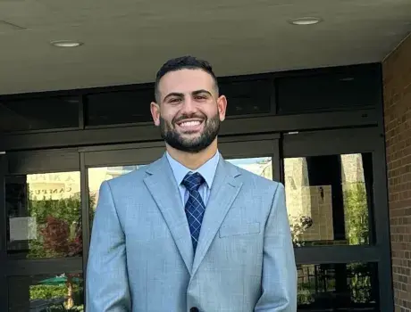 Medium shot of Zaki Farah wearing a suit and tie in front of the law school building.