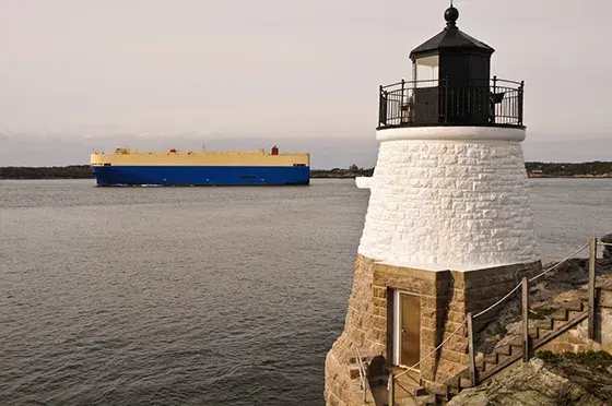 a lighthouse in foreground with container ship on calm waters in background