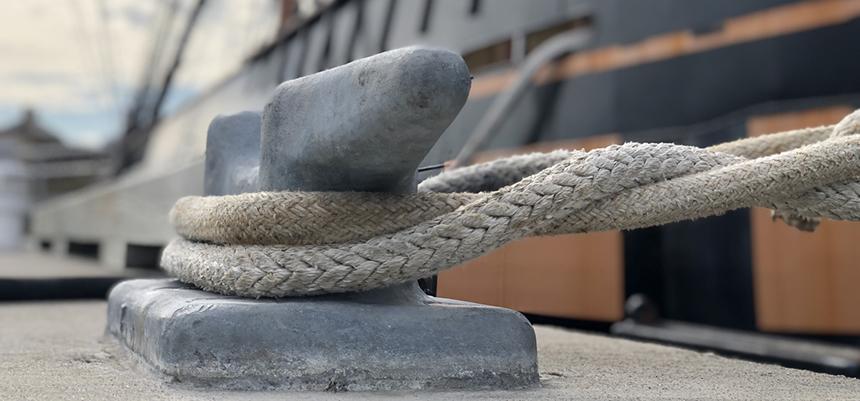 image of a closeup of a clete wrapped with a rope securing a large vessel to a dock