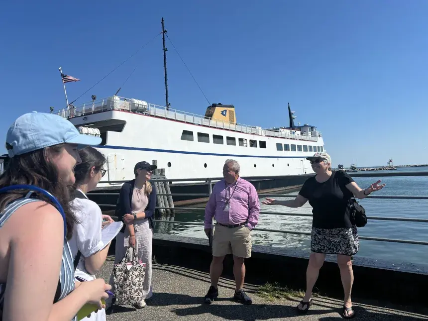 Small group of students at the coast with a white ship in the background.
