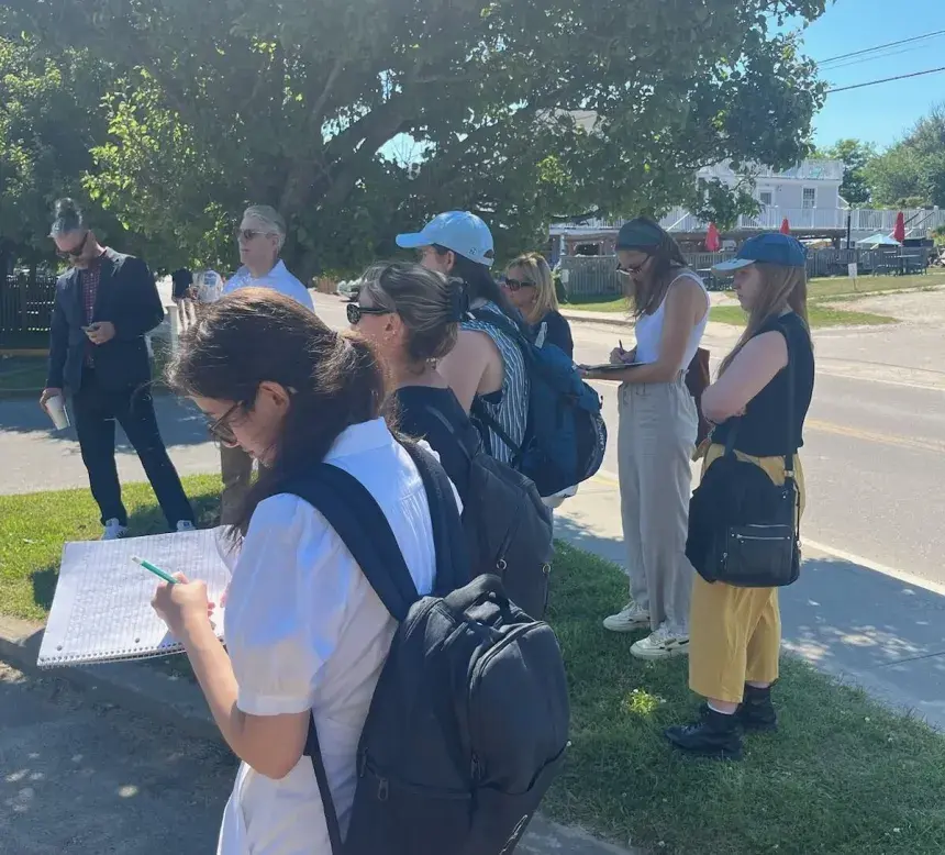 Students taking notes, standing by trees. 